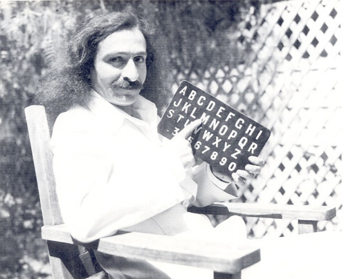 Photo of Meher Baba with His right hand pointing to the letter M on His alphabet board